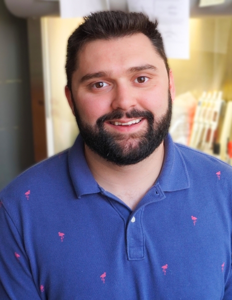 Man with black hair and beard wearing a blue polo in a lab setting